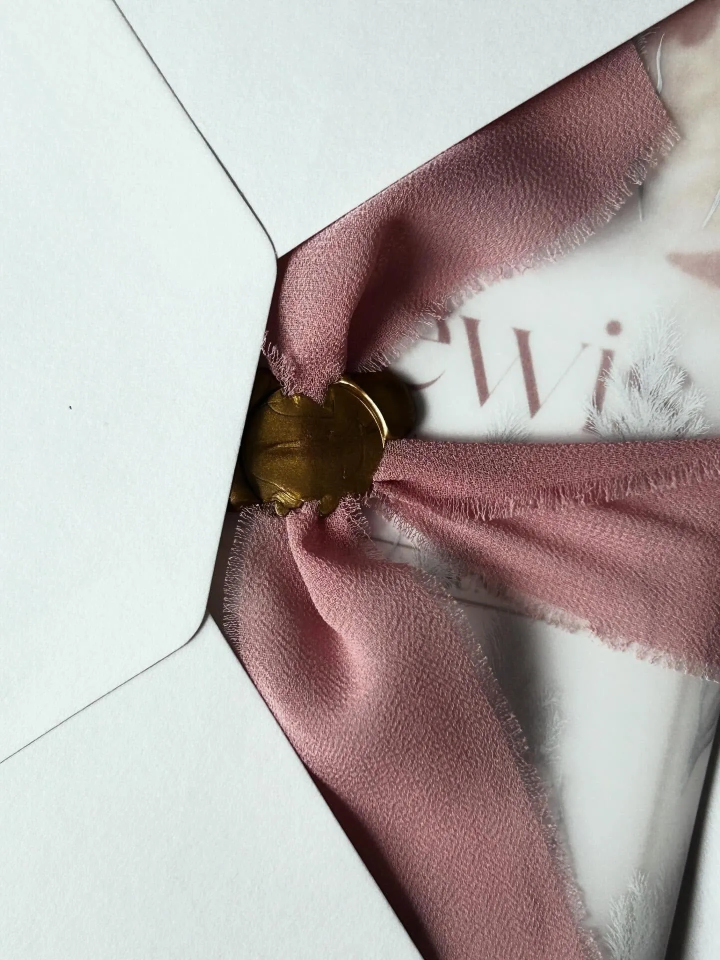 A bespoke invitation suite in its vellum wrap with blush silk ribbon and gold wax seal, on deep red velvet.
