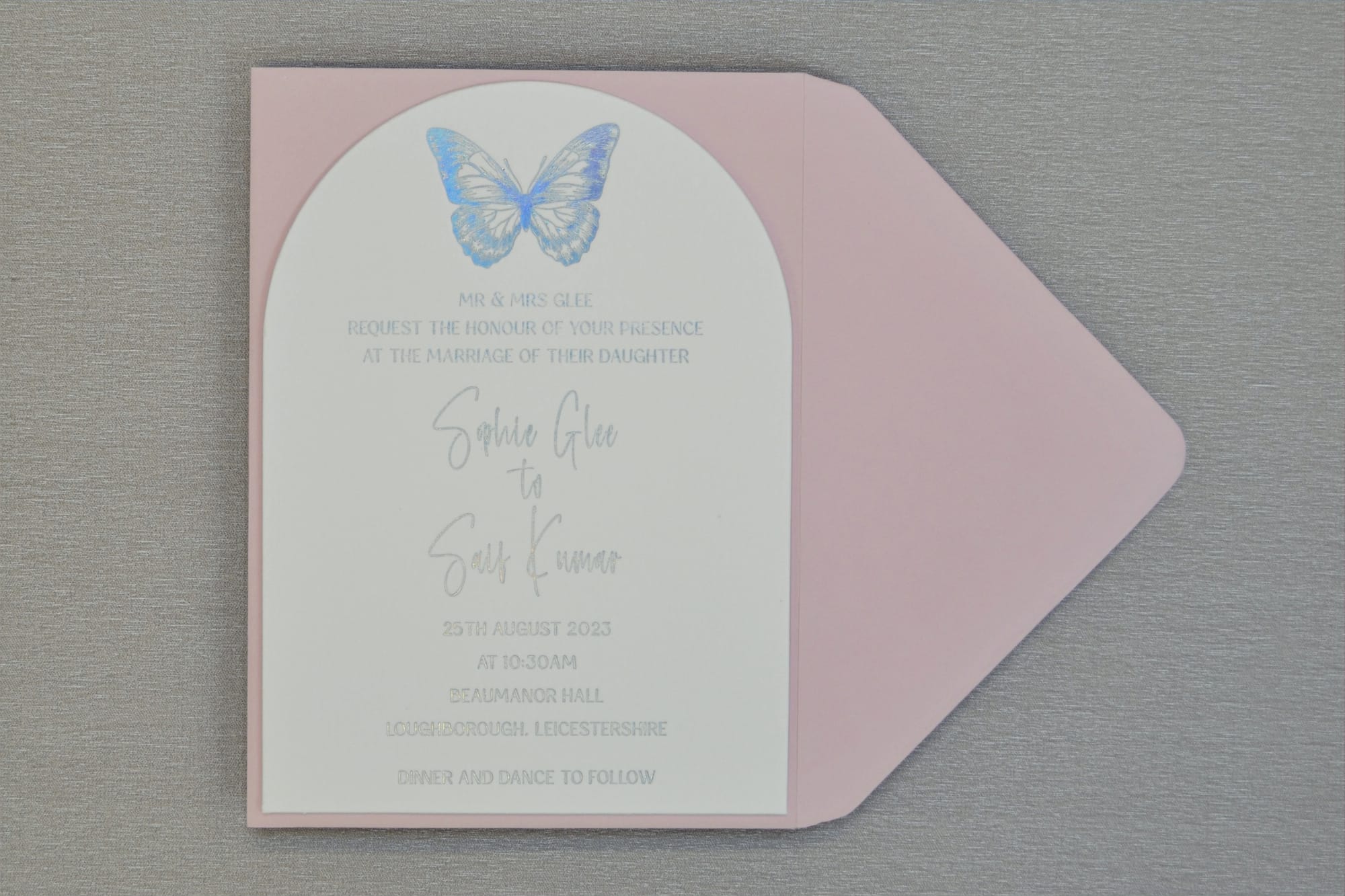 Arched Butterfly Collection invitation on a blush envelope, with a blue foiled butterfly above silver foiled wording for a wedding at Beaumanor Hall.
