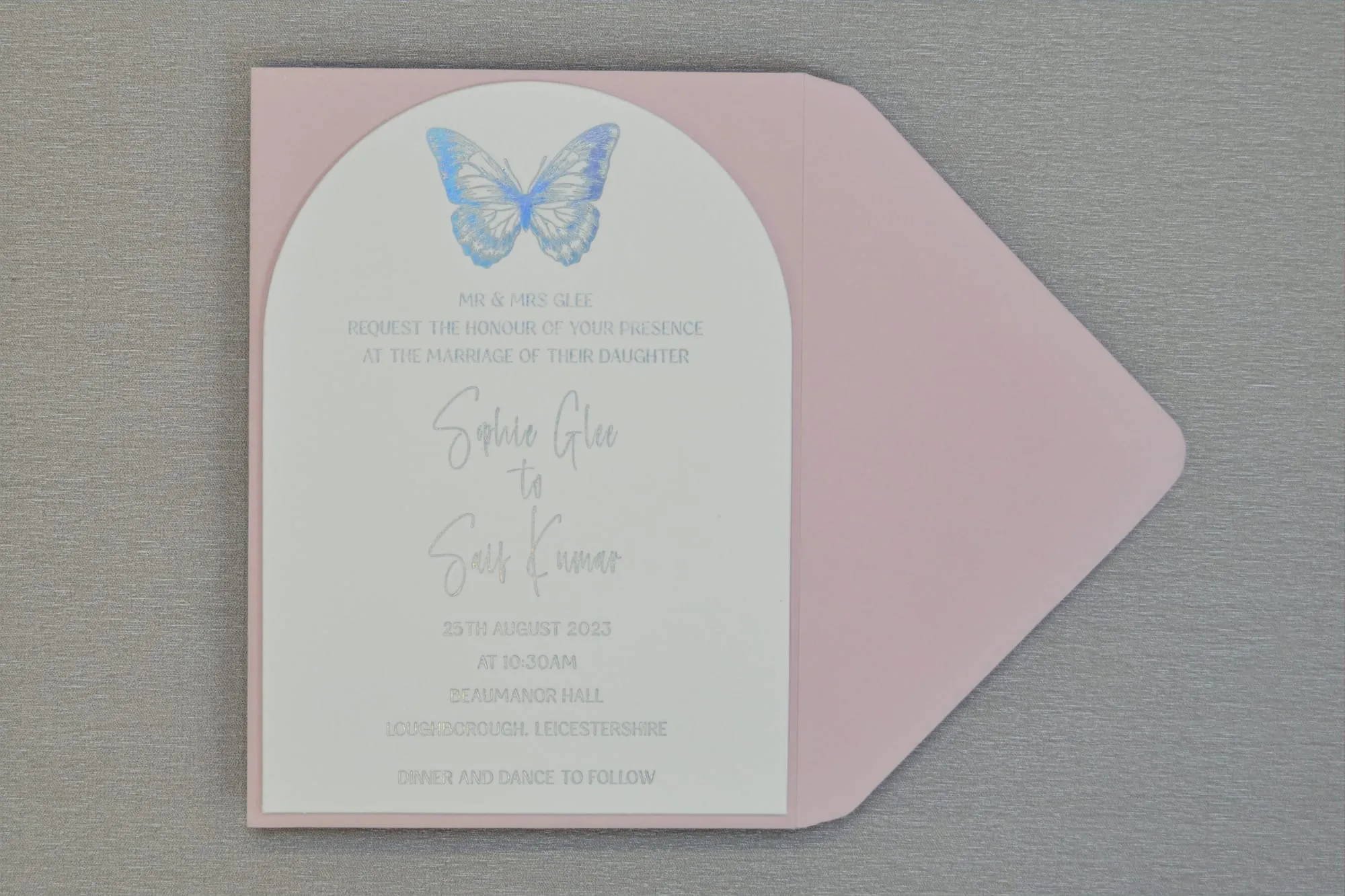 Arched Butterfly Collection invitation on a blush envelope, with a blue foiled butterfly above silver foiled wording for a wedding at Beaumanor Hall.