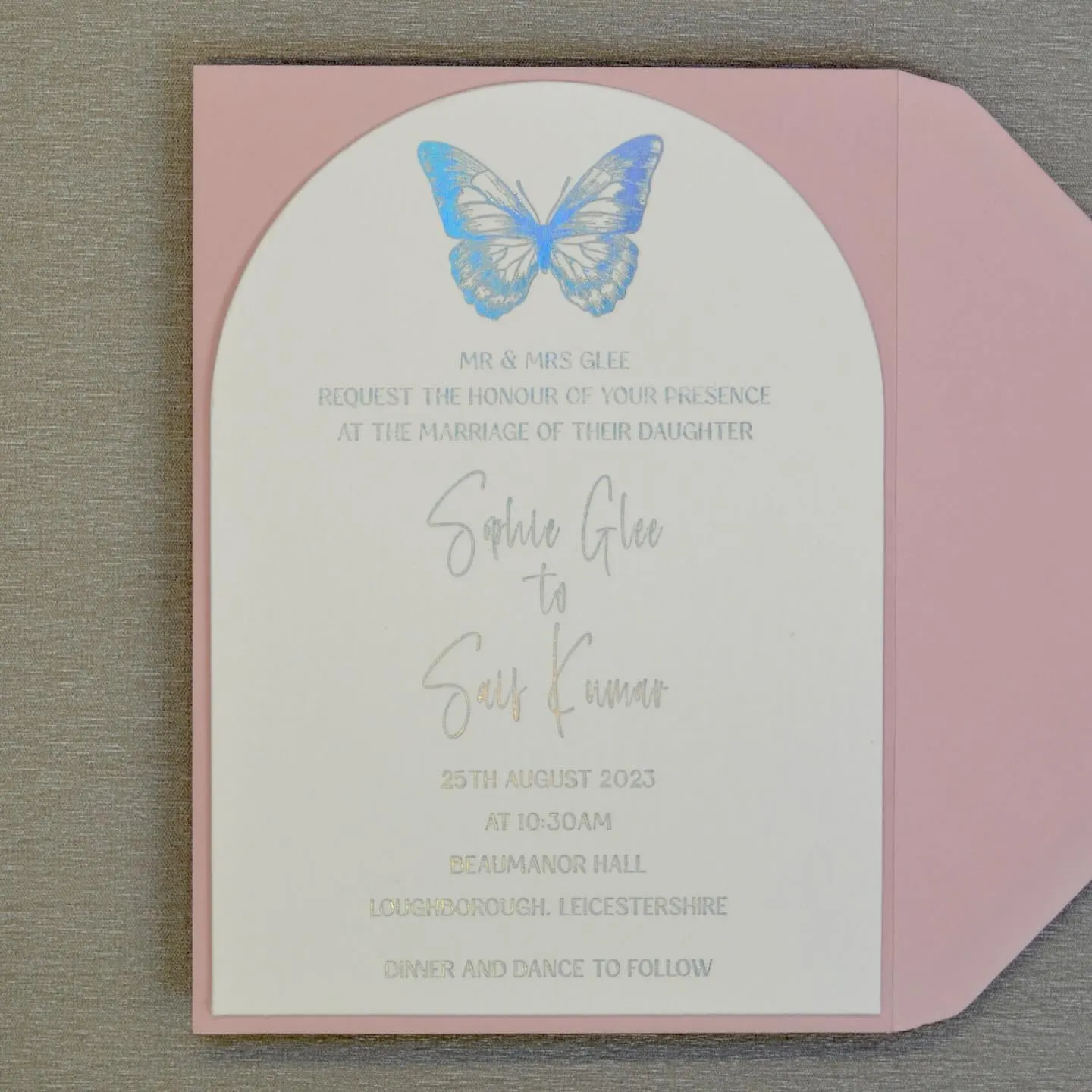 The arched Butterfly invitation resting on its blush envelope, showing the gold foiled venue details.